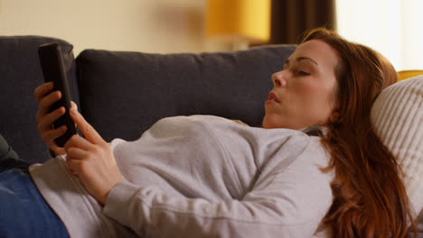 Close-Up-Of-Woman-Lying-On-Sofa-At-Home-At-Streaming-Or-Watching-Movie-Or-Show-Or-Scrolling-Internet-On-Mobile-Phone-6